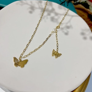 Collier papillon doré élégant avec perle blanche sur fond de plateau en céramique