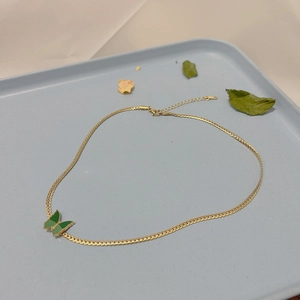 Détail du collier chaîne serpent dorée avec un pendentif papillon en émail vert