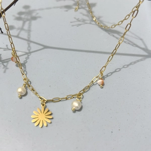 Gold chain necklace featuring daisy pendant, white pearls and striped beads on grey background