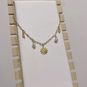 Detail of gold daisy pendant necklace with white pearls and pink cat eye beads on stand