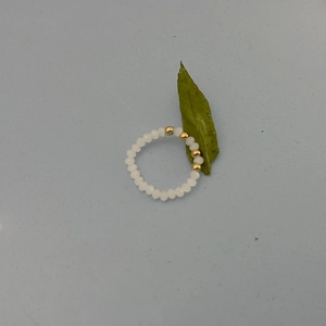 Close-up of beaded ring with white resin pearls and gold metal beads on grey surface