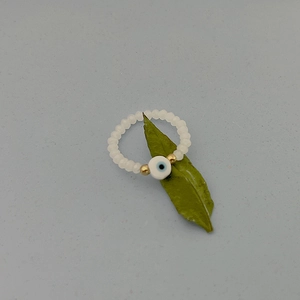 Macro detail of a beaded evil eye ring featuring white faceted beads and gold accents