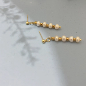 Detail of freshwater pearl tassel earrings with gold beads on a soft grey background