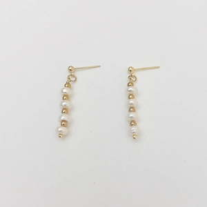 Macro detail of 925 silver needle pearl tassel earrings with gold beads on white background