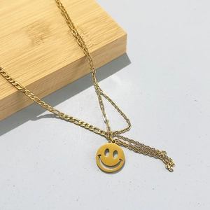 Close-up of layered gold necklace with smile pendant on a wooden block and grey background