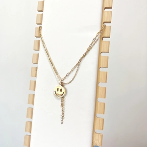 Detail of 18K gold plated layered smile pendant necklace with tassel on a display stand