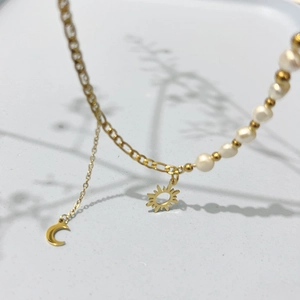 Détail des pendentifs soleil et lune sur un collier asymétrique en perles dorées