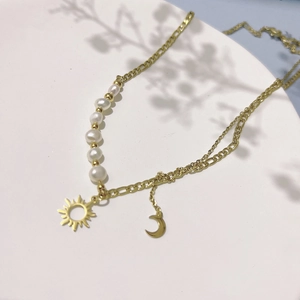 Détail du collier doré double épaisseur avec accents de perles et breloques soleil lune