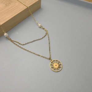 Détail du pendentif soleil doré avec doubles perles blanches sur chaîne en acier inoxydable