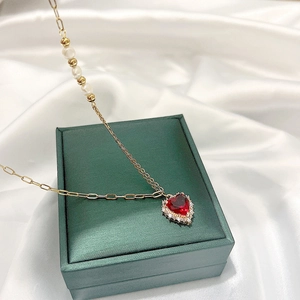 Collier coeur doré avec gemme rouge, perles et cristaux sur un fond de soie fine