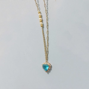Détail du pendentif cœur bleu avec perles blanches sur une chaîne dorée fine