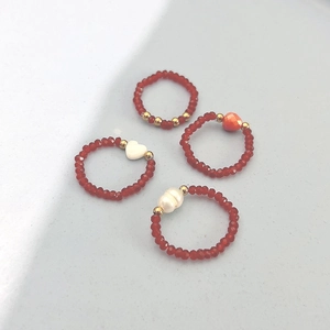 Handmade red crystal bead rings set with pearls and shell heart charms on stone background