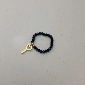 Detail van elastische ring met zwarte gefacetteerde kralen en goudkleurige hart-sleutel hanger