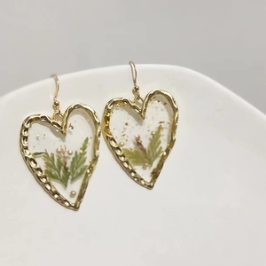 Makro-Detail von 18K Gold-Herzohrringen mit grünen Trockenblumen und Perlen