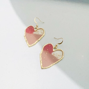 Macro detail of 18K gold titanium heart earrings with pink resin and gold leaf inlay
