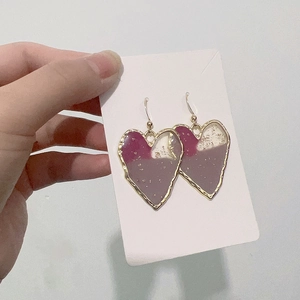 Detail of gold-plated heart earrings featuring pink resin inlay and delicate gold foil flakes