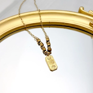 Detailed close-up of retro 18K gold evil eye pendant and beaded chain on mirror