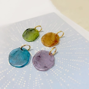 Detail of four colorful resin disc earrings with gold hoops in green amber blue and purple