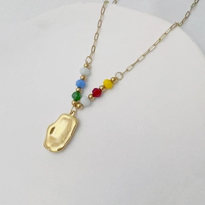 Detail of gold necklace featuring irregular metal pendant and five colorful resin beads