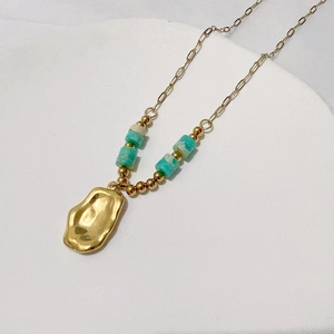 Detail of gold beaded necklace featuring turquoise cylinders and irregular molten pendant