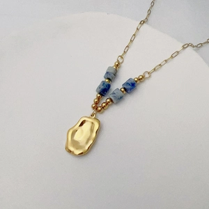 Detail of gold textured wavy pendant with blue marble beads on a minimalist necklace