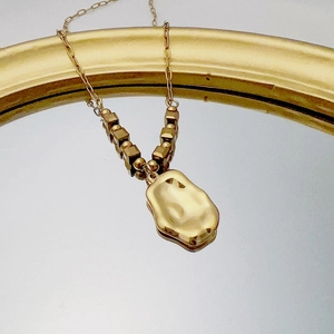 Macro shot of liquid metal gold pendant with cube beads on a mirrored surface