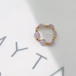 Detail of beaded ring with pink heart crystals and gold beads on white paper