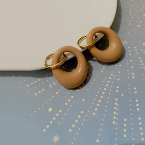 Λεπτομέρεια από χρυσά σκουλαρίκια 18K με μπεζ μενταγιόν ρητίνης σε λευκή πορσελάνη