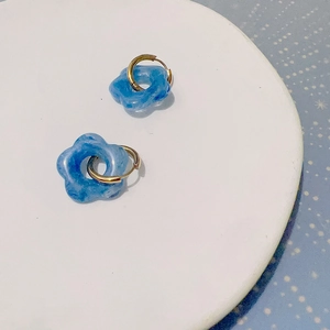 Détail macro de boucles d'oreilles fleur en résine bleue avec anneaux dorés sur plateau