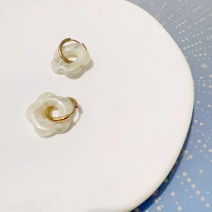 Détail de breloques fleurs en acrylique blanc sur des boucles d'oreilles créoles dorées