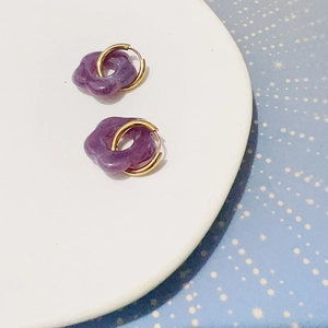 Vue détaillée de boucles d'oreilles fleur en résine violette avec anneaux dorés sur plateau