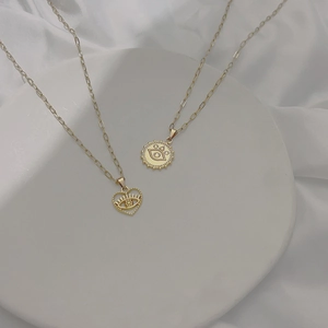 Dettaglio di collane in oro 18k con pendenti a cuore e malocchio su vassoio bianco
