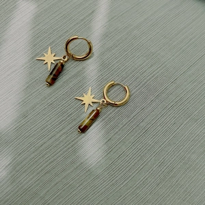 Détail de boucles d'oreilles étoiles dorées avec pierres naturelles œil de tigre