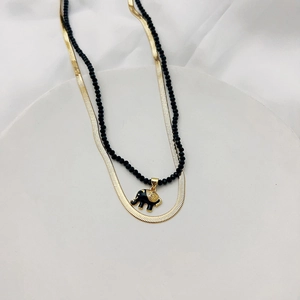 Detail of a layered gold snake chain and black beaded necklace with elephant pendant
