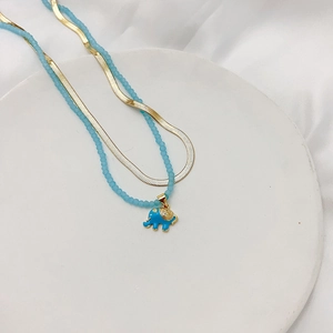 Gold layered necklace with blue beads and elephant pendant on a white silk background