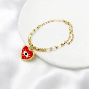 Détail d'un bracelet doré avec cœur en émail rouge et breloque œil de démon sur soie