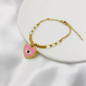 Détail du bracelet doré avec cœur en émail rose, œil protecteur et perles en verre