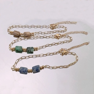 Three gold-plated link bracelets with square natural stones on a mirror surface