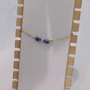 Detail of gold chain bracelet with square blue natural stones on a white display stand