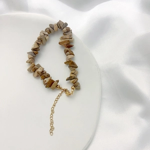 Close-up of bohemian natural stone bracelet with gold plated clasp on white silk fabric
