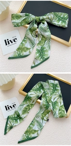 Détail d'un long foulard en soie à imprimé tropical vert noué en ruban sur fond beige