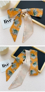 Détail d'un foulard en soie orange vif avec motif de feuilles tropicales noué en nœud