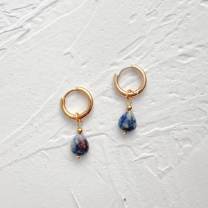 Detail of 18k gold drop earrings with natural teardrop stones on stone background