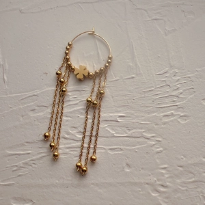Macro shot of 18K gold clover earring featuring elegant beaded tassel chains on white stone