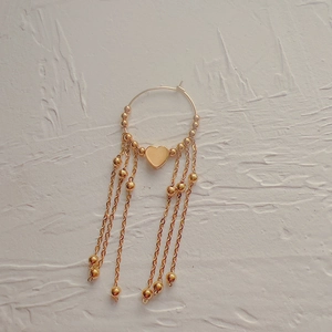 Detail of 18K gold-plated heart earring with elegant beaded tassel chain on white wall