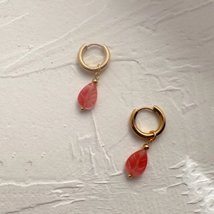 Détail de boucles d'oreilles en acier doré 18K avec pendentifs feuille en pierre rose