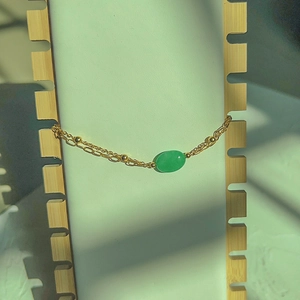 Close-up of double-layered gold chain bracelet with oval green gemstone on a white stand