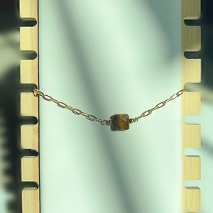 Détail du bracelet chaîne trombone dorée avec une pierre oeil de tigre carrée