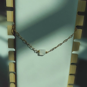 Détail d'un collier chaîne dorée minimaliste avec pendentif carré blanc sur présentoir