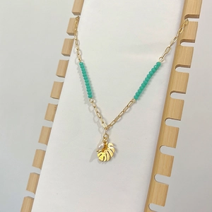 Close-up of tropical gold necklace with green beads, monstera leaf pendant, and white pearl